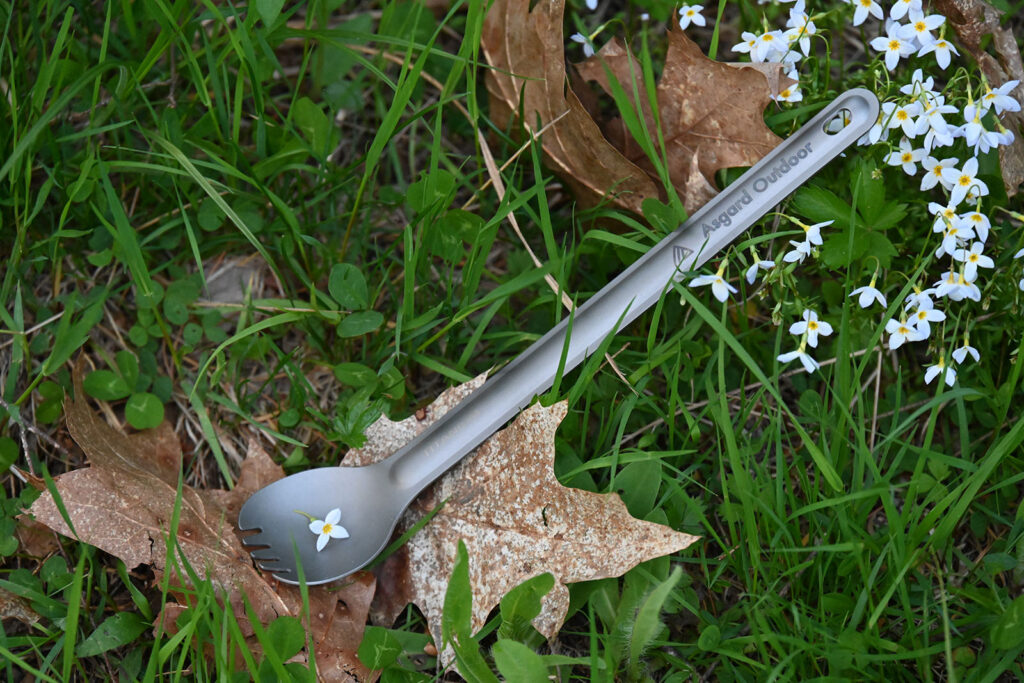Asgard Titanium Spork resting on grass with wildflowers