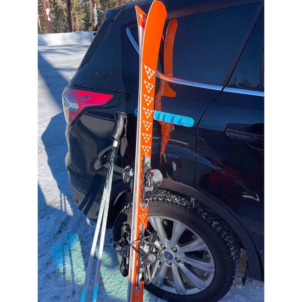 Blue Asgard Pill attached to black SUV with orange skis and ski poles leaning beside the vehicle
