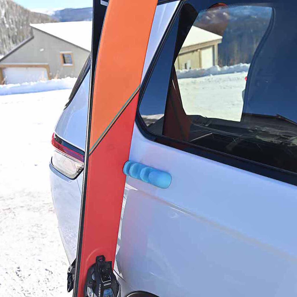 Blue Asgard Pill attached to white vehicle with orange snowboard leaning against parked car in snow