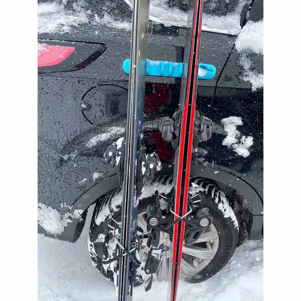 Blue Asgard Pill attached to black vehicle with skis leaning beside it in a snowy parking lot