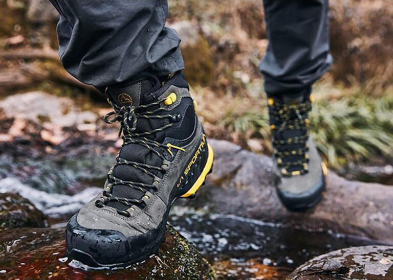 A hiker in waterproof boots crosses a stream on rocks