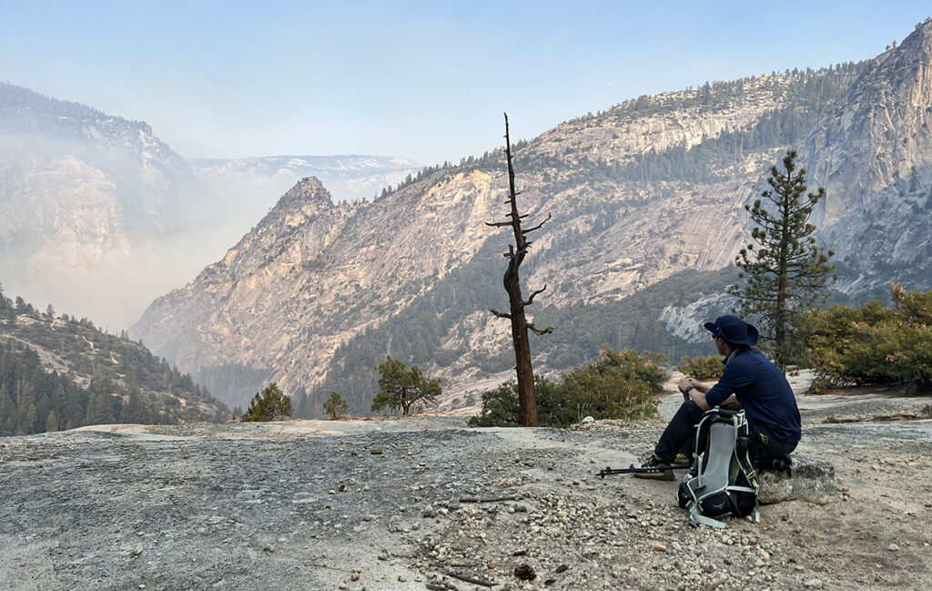A hiker in hiking boots on a rock with a backpack, overlooking a mountain valley