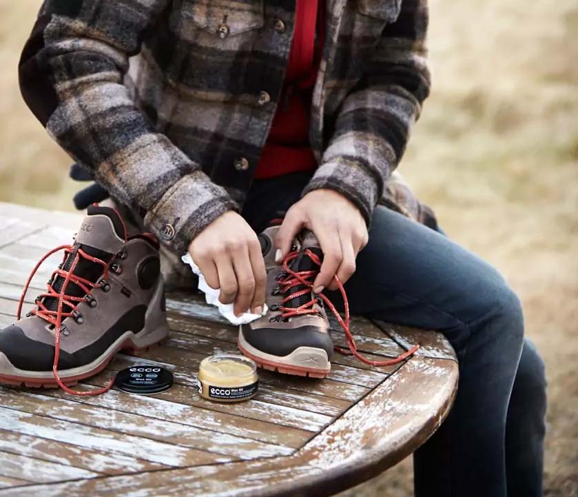 A woman cleaning hiking boots with wax on a wooden table