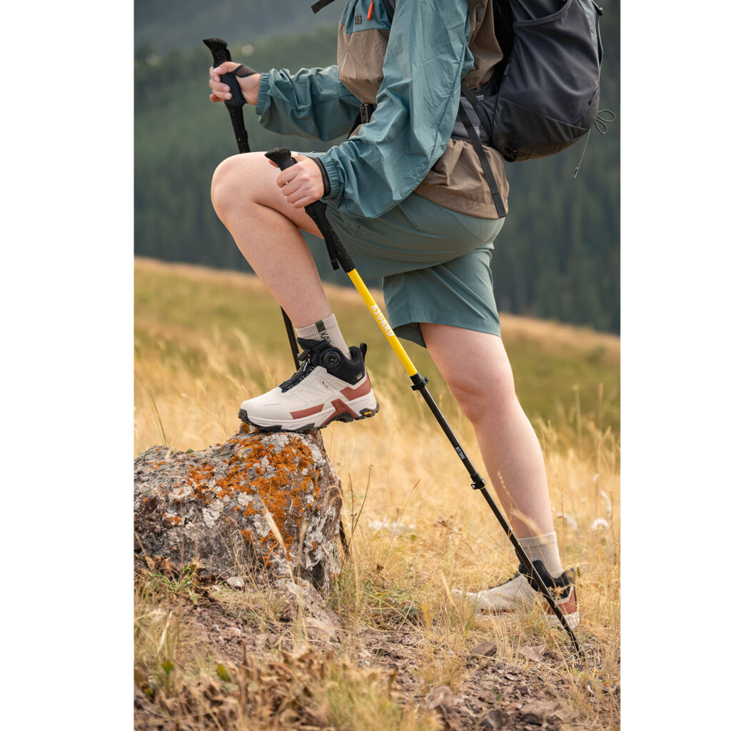 Hiker using Asgard Hydrogen Poles 2.0 while stepping on a rock in grassy mountain terrain
