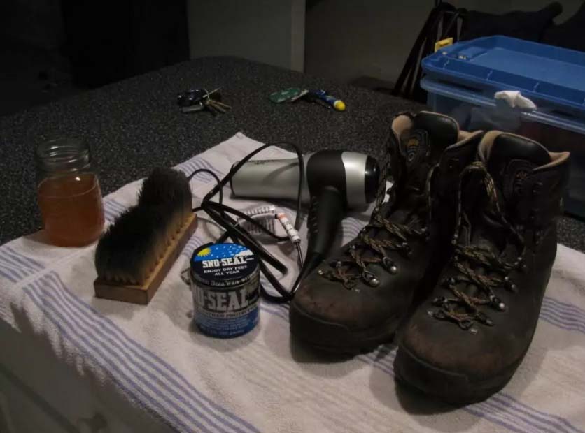Hiking boots with cleaning tools on a towel, including a brush and hairdryer