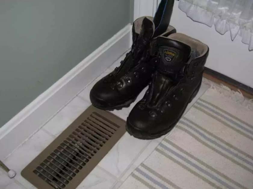Black hiking boots drying on a floor vent near a door
