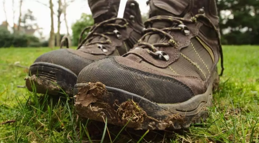 Muddy brown hiking boots on green grass in a field