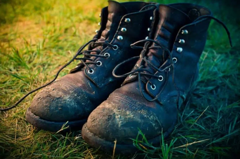 A pair of muddy black hiking boots with laces, placed on green grass