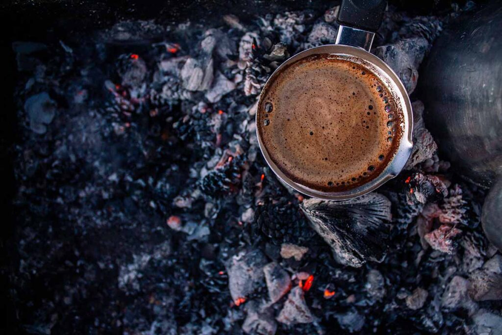 A cup of coffee on hot coals from a campfire