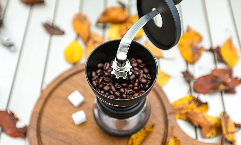 Manual coffee grinder filled with coffee beans on a wooden board