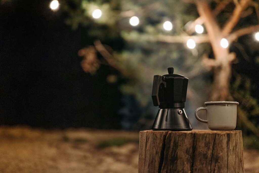 A moka pot and cup on a tree stump under string lights at night