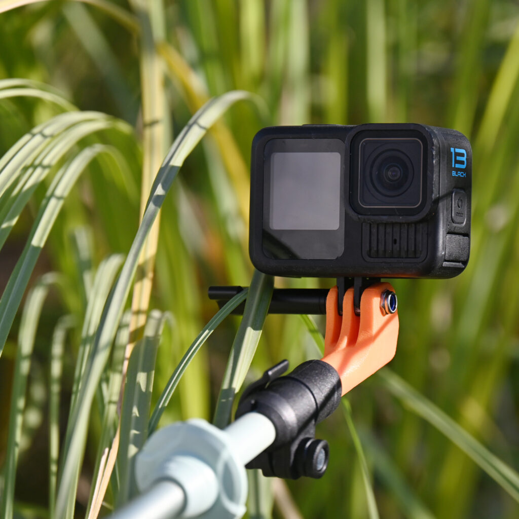 Black GoPro camera mounted on an orange Asgard mount, set against a blurred green natural background.