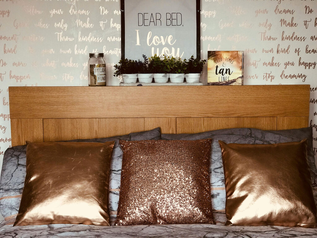 Bed with gold and sequin pillows, wooden headboard, and wall art