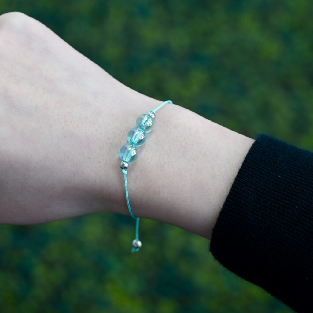Close-up of Asgard Alpine ID translucent cyan bracelet worn on wrist with three translucent cyan beads and matching adjustable cord.