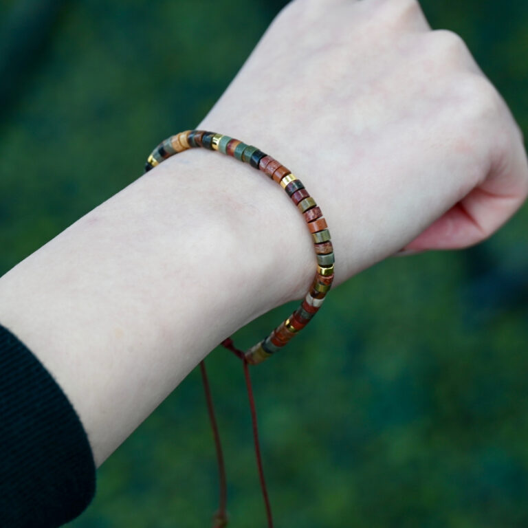 Asgard Terra ID earth-tone mineral bracelet worn on wrist, showing slim multicolor disc beads and adjustable brown cord.