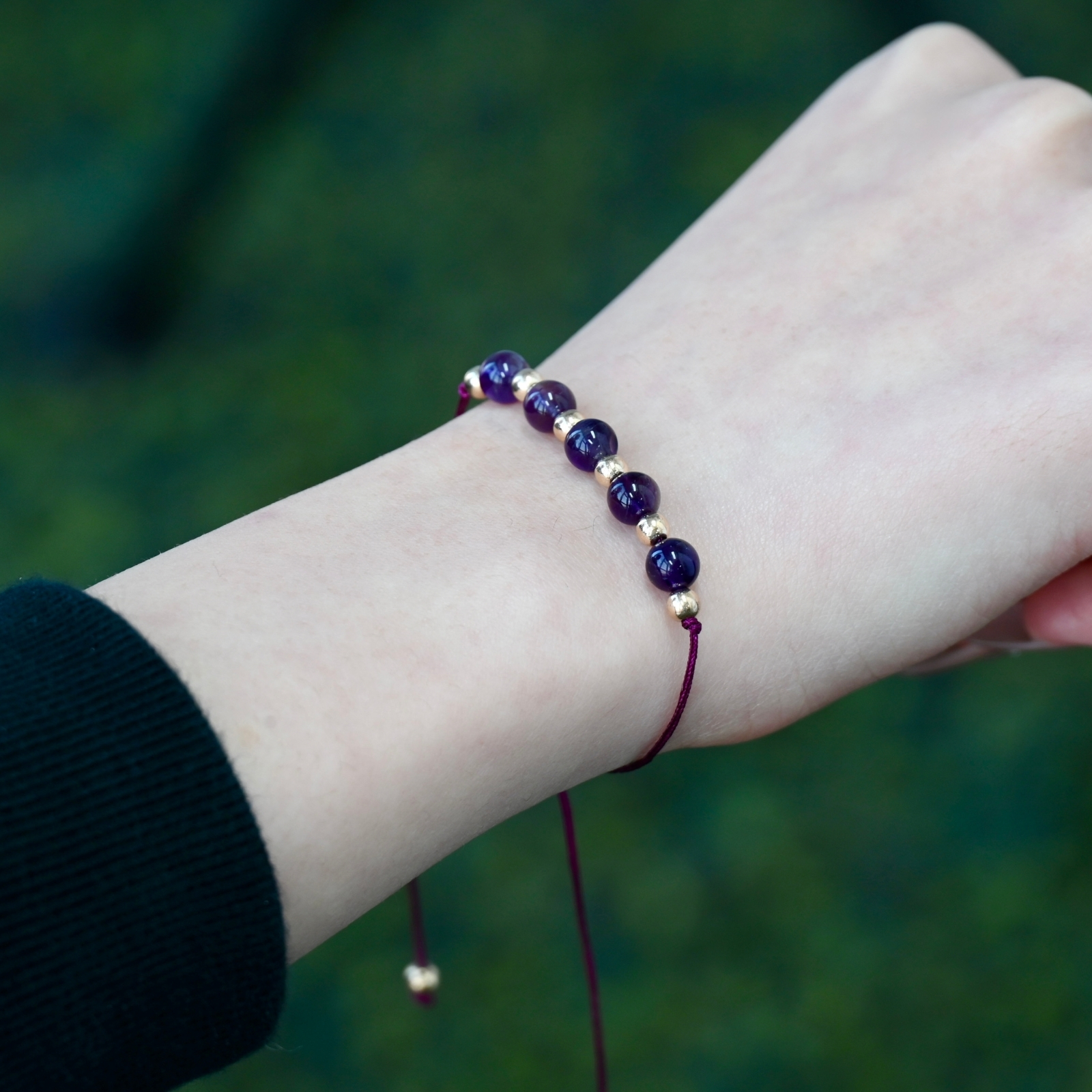 Close-up of the Asgard Twilight ID bracelet worn on a wrist with deep purple beads, gold accents, and a plum adjustable cord.