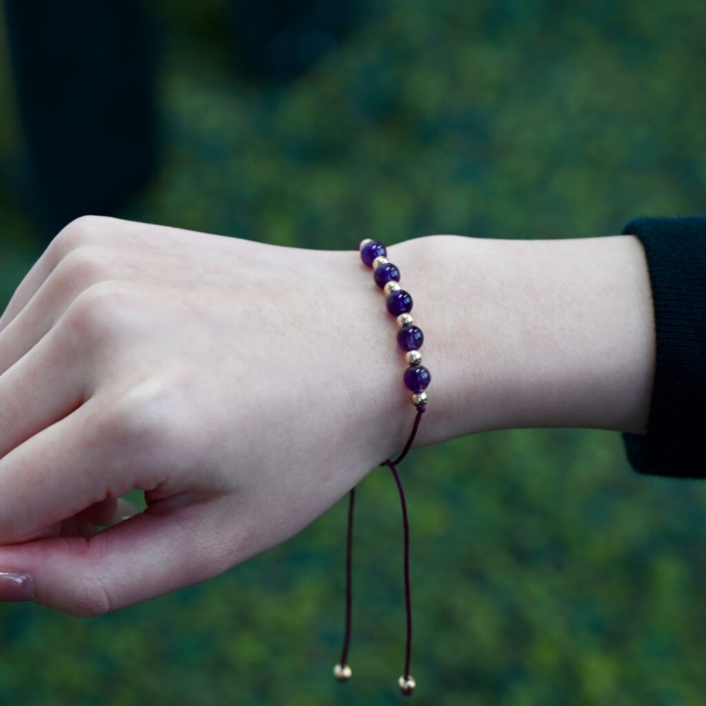 Asgard Twilight ID bracelet worn outdoors with deep purple beads, gold accents, and long plum adjustable cords.