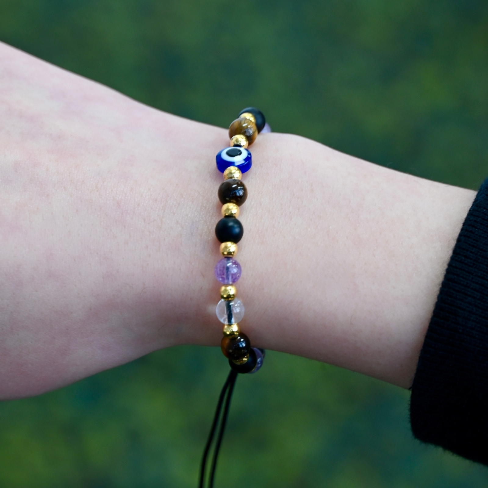 Person wearing the Asgard Vigil ID natural stone bracelet with brown, black, clear, and violet beads, gold-tone spacers, and a blue eye-style focal bead.