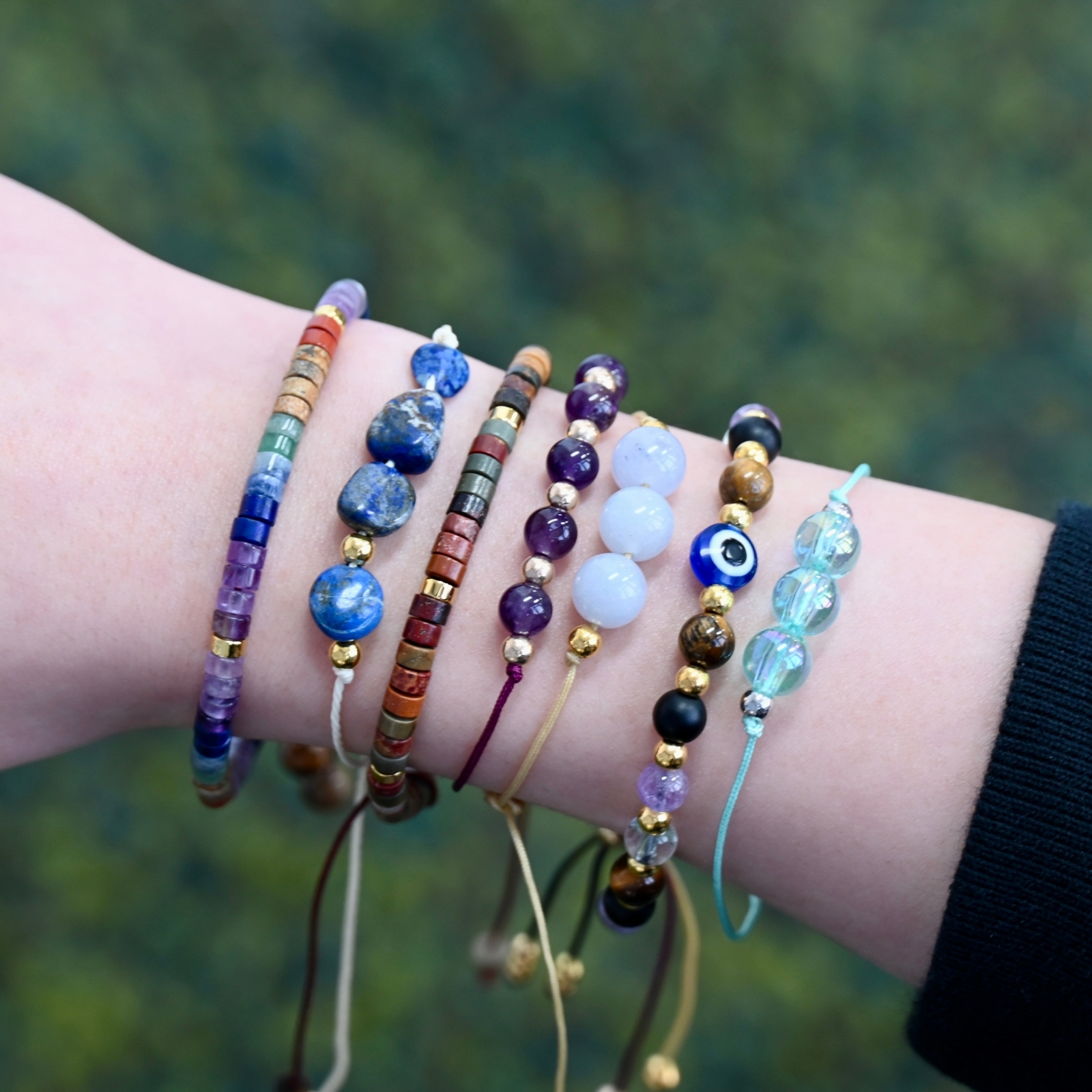 Close-up of a wrist wearing multiple colorful natural stone trail bracelets with adjustable cords outdoors