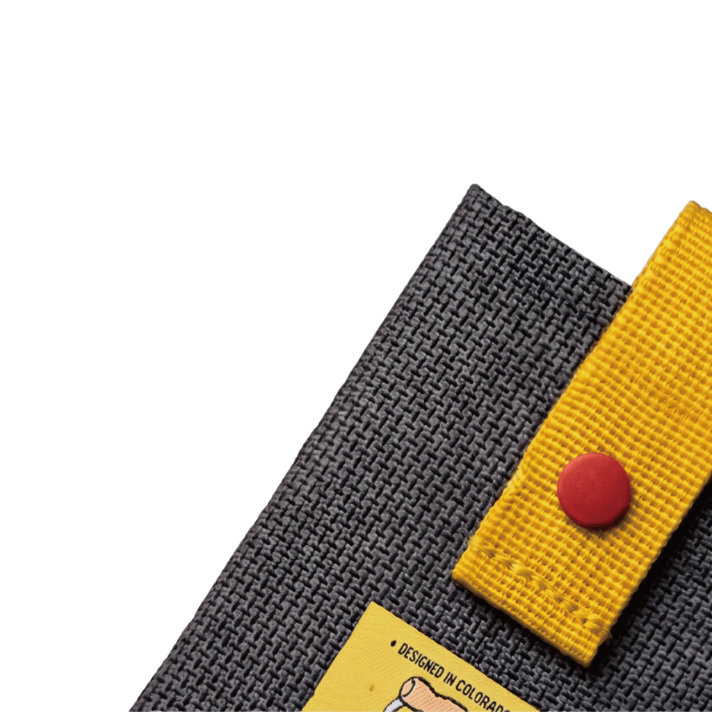 Angled close-up of dark gray card holder fabric beside a yellow strap and red snap.