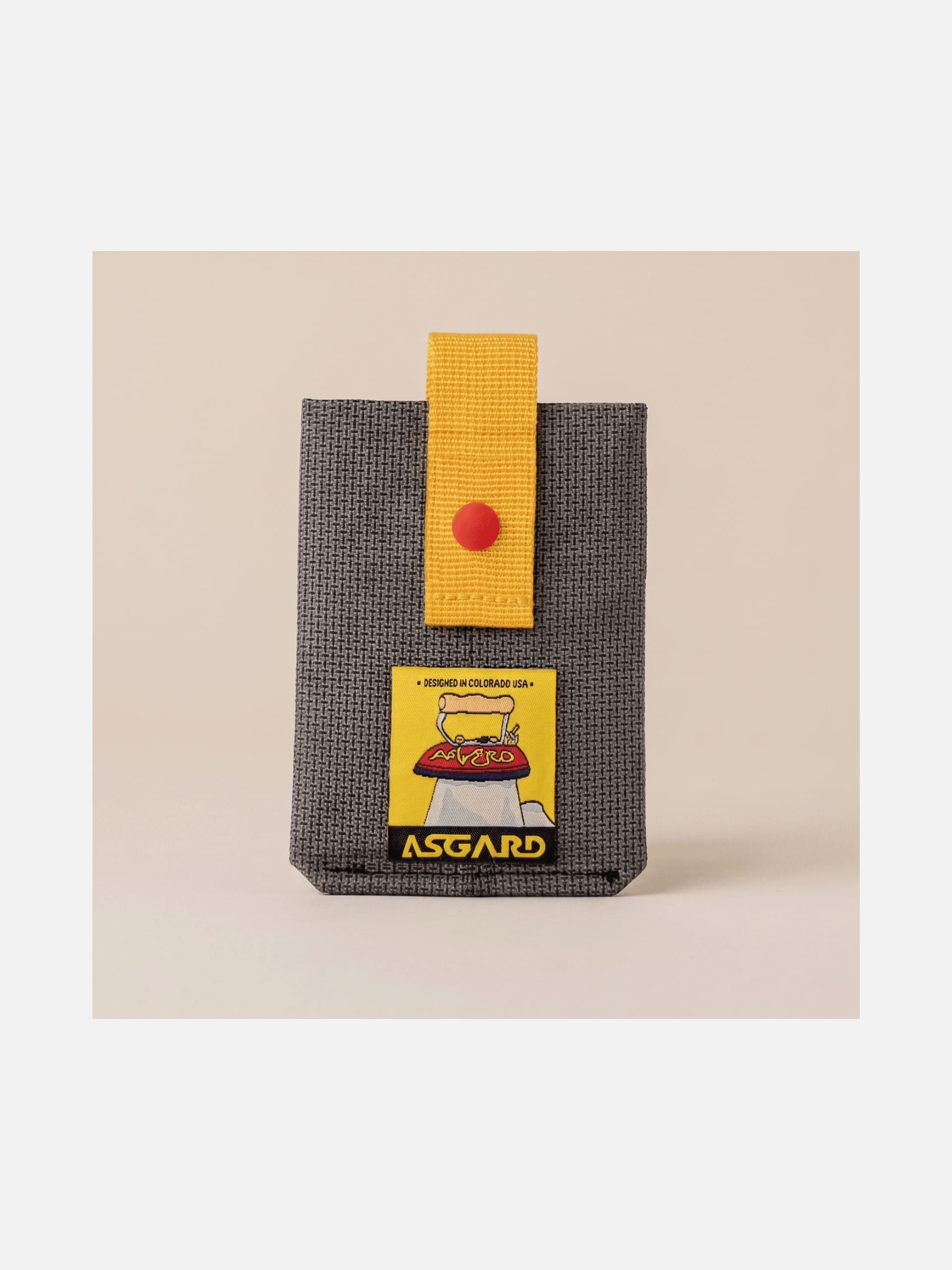 Asgard card holder standing upright on a beige surface, showing dark gray fabric and a yellow strap.