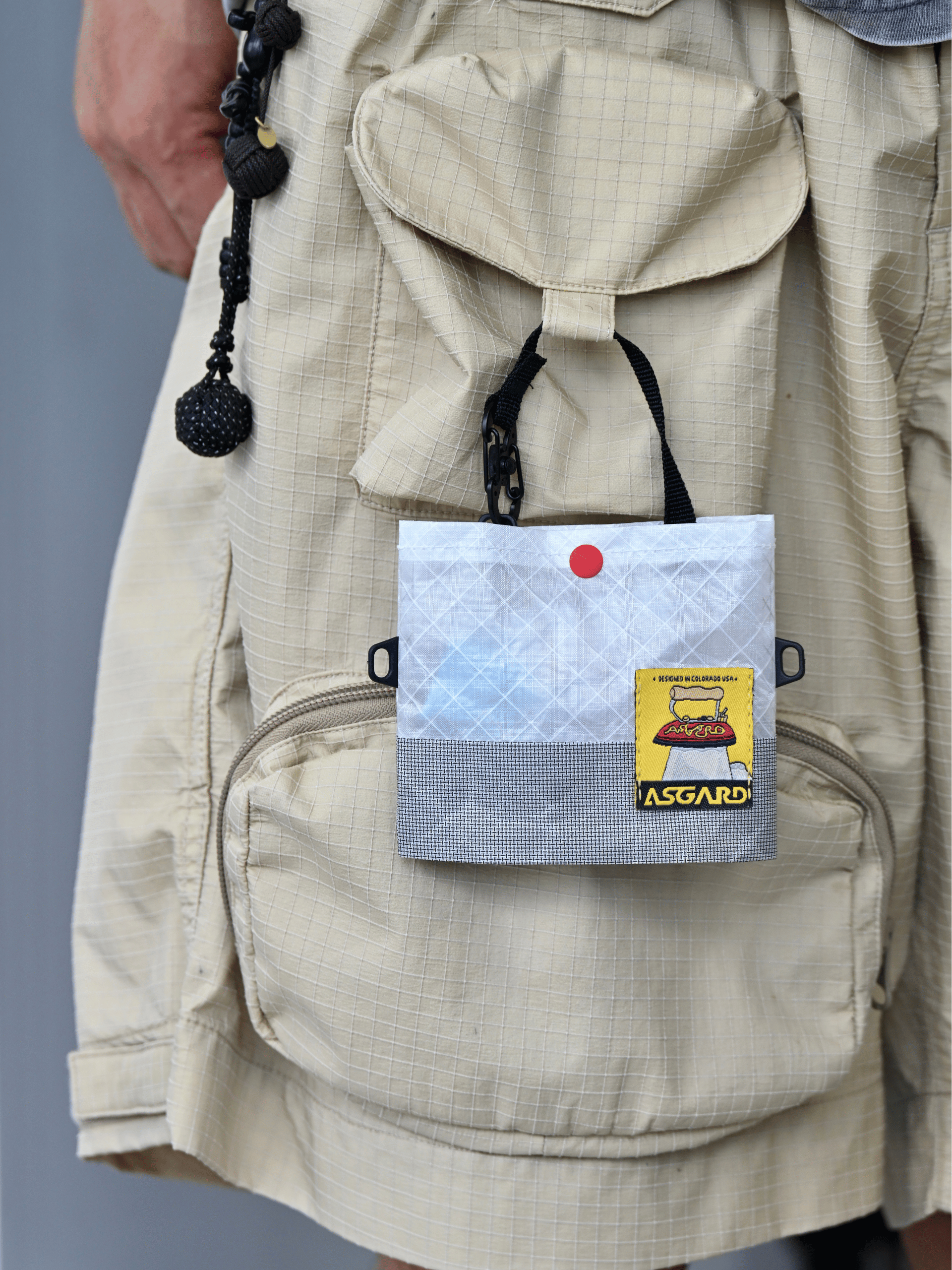 Light gray Asgard Mini Tote Bag attached to a pocket loop on beige cargo shorts.