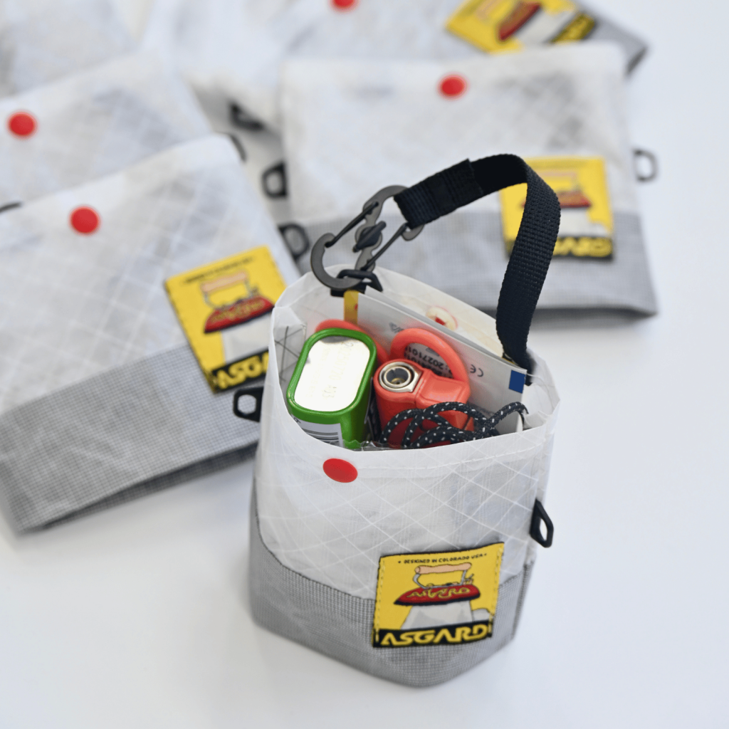Open Asgard mini tote holding small everyday items, with its black handle and snap hook raised.