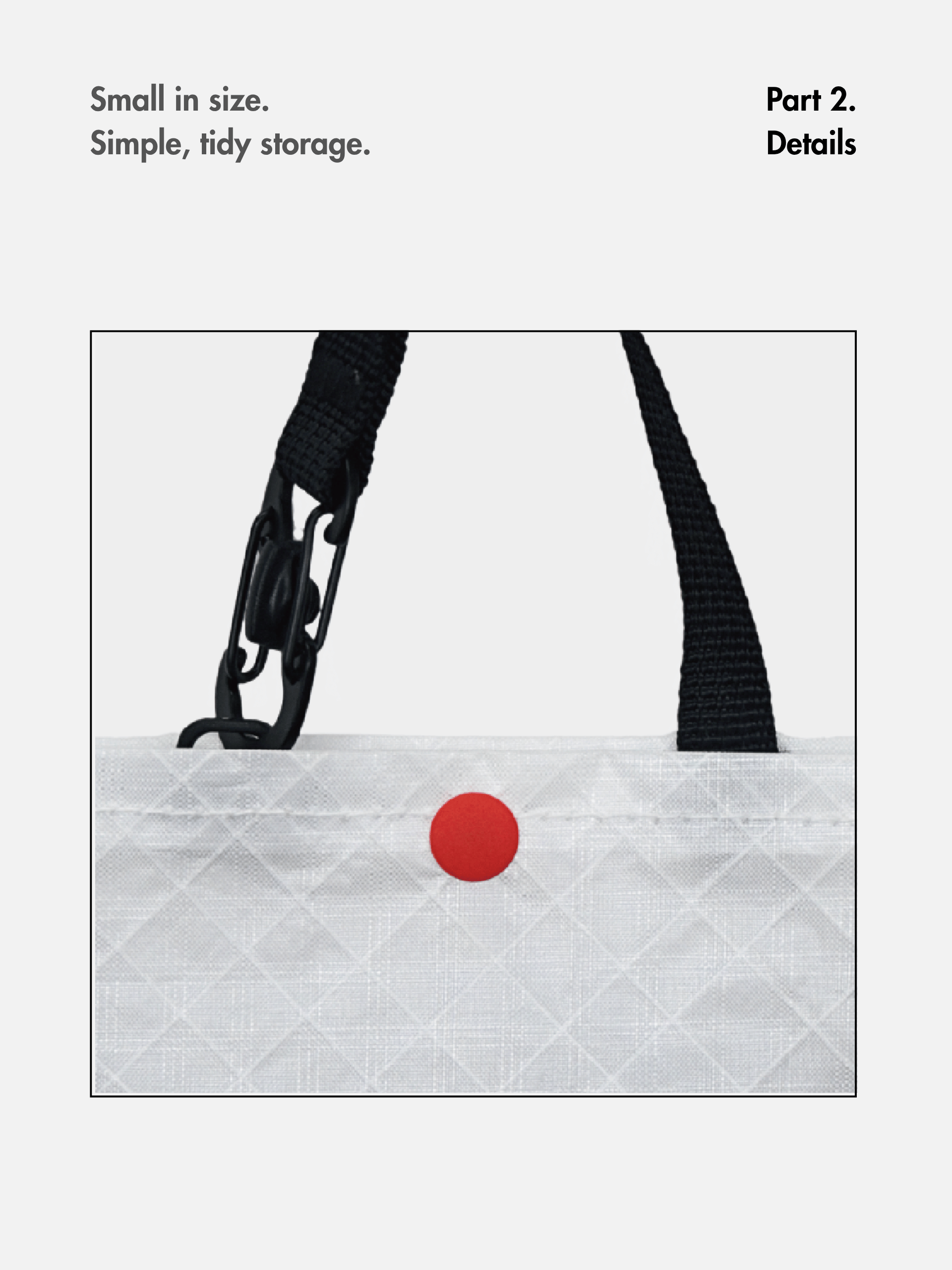 Close-up of the mini tote’s black handle, snap hook and red snap closure on light gray fabric.