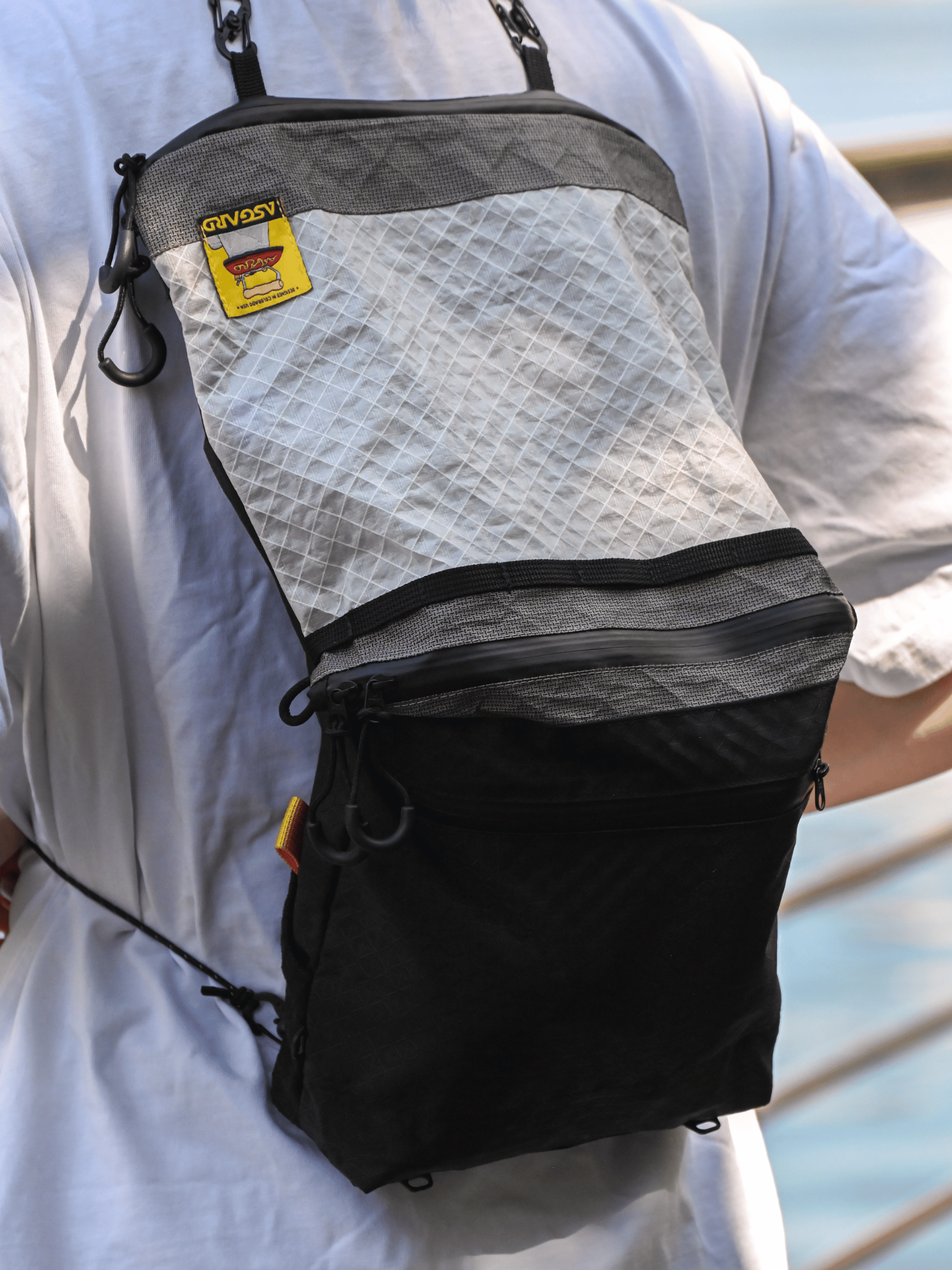 Close-up of the Asgard Versa Bag 5L worn as a backpack over a white T-shirt, with its white and black panels fully extended.