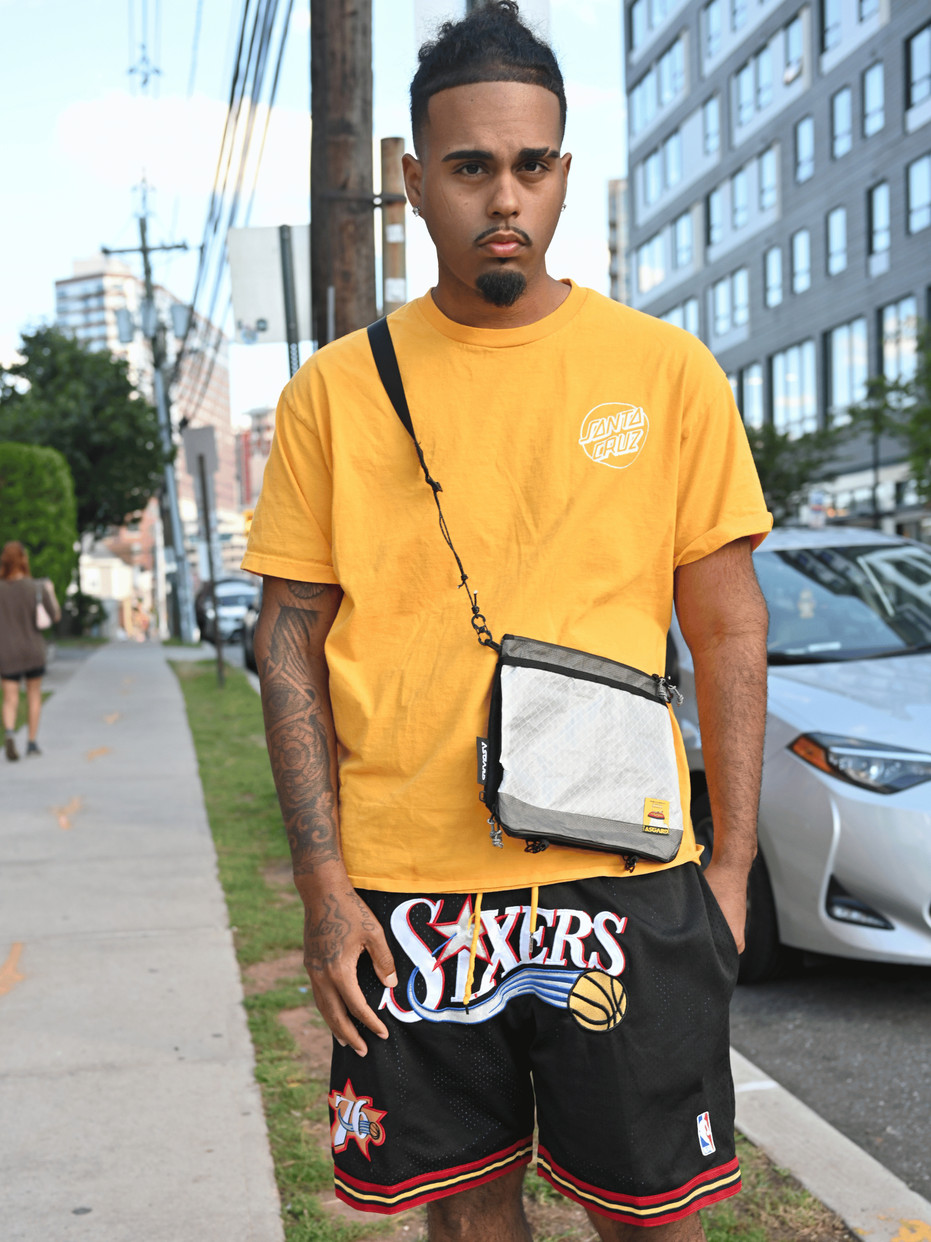 Man in a yellow T-shirt wearing the white Asgard Versa Bag 5L crossbody on a city sidewalk.