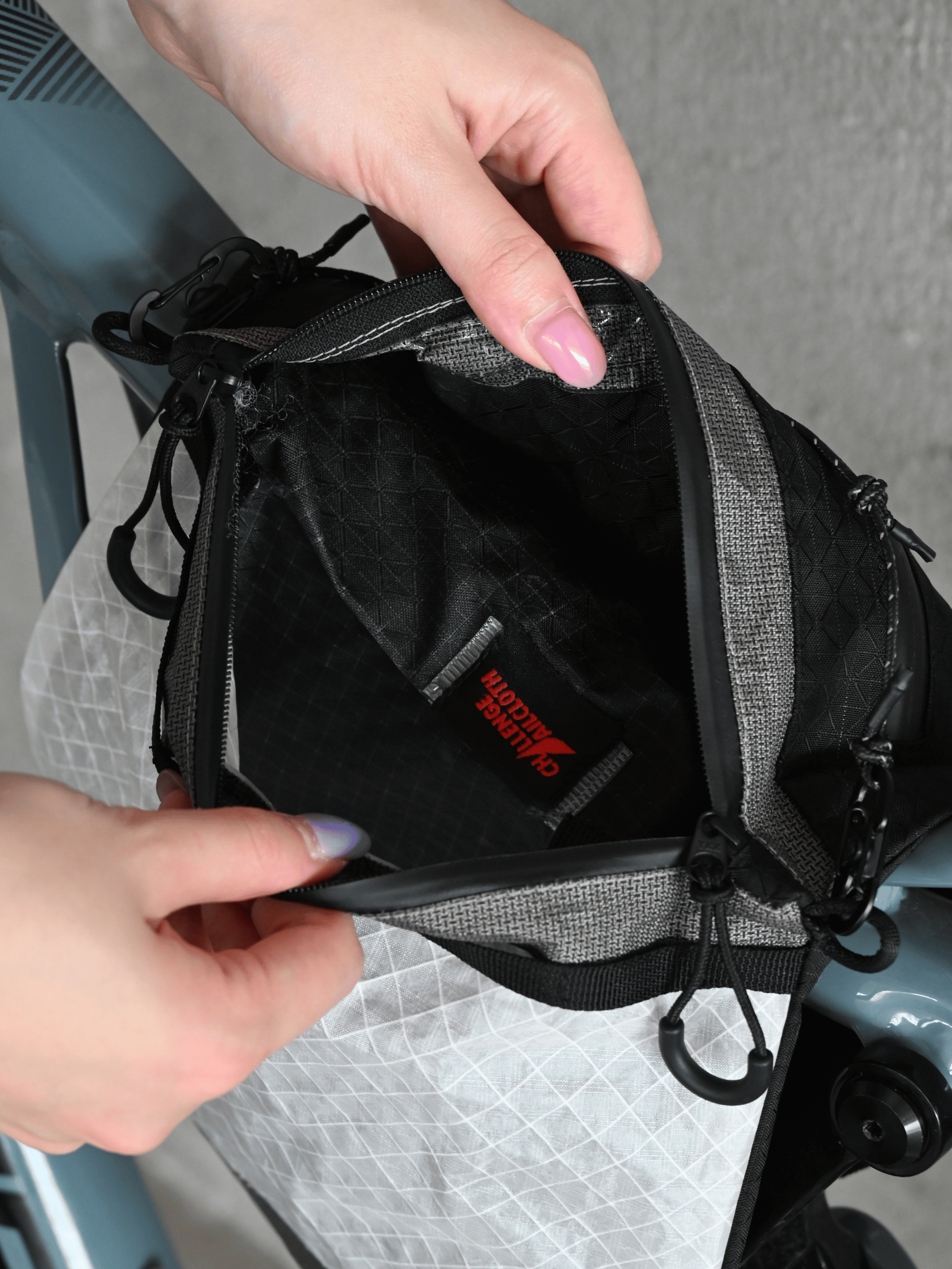 Hands opening the Asgard Versa Bag 5L to show its black interior, stitched seams and Challenge Sailcloth label.
