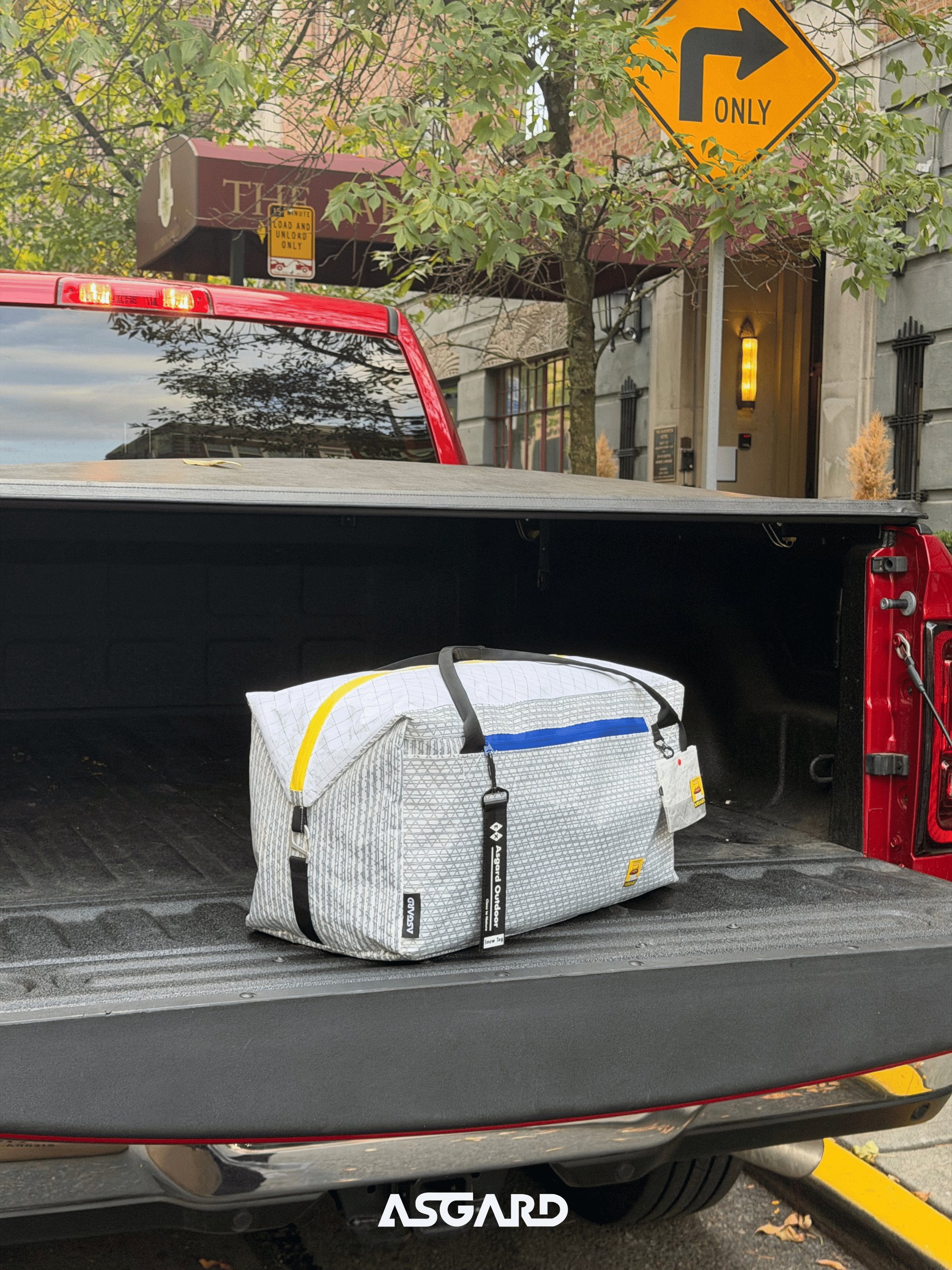 Asgard Duffel Bag resting on an open pickup tailgate beside a tree-lined street.