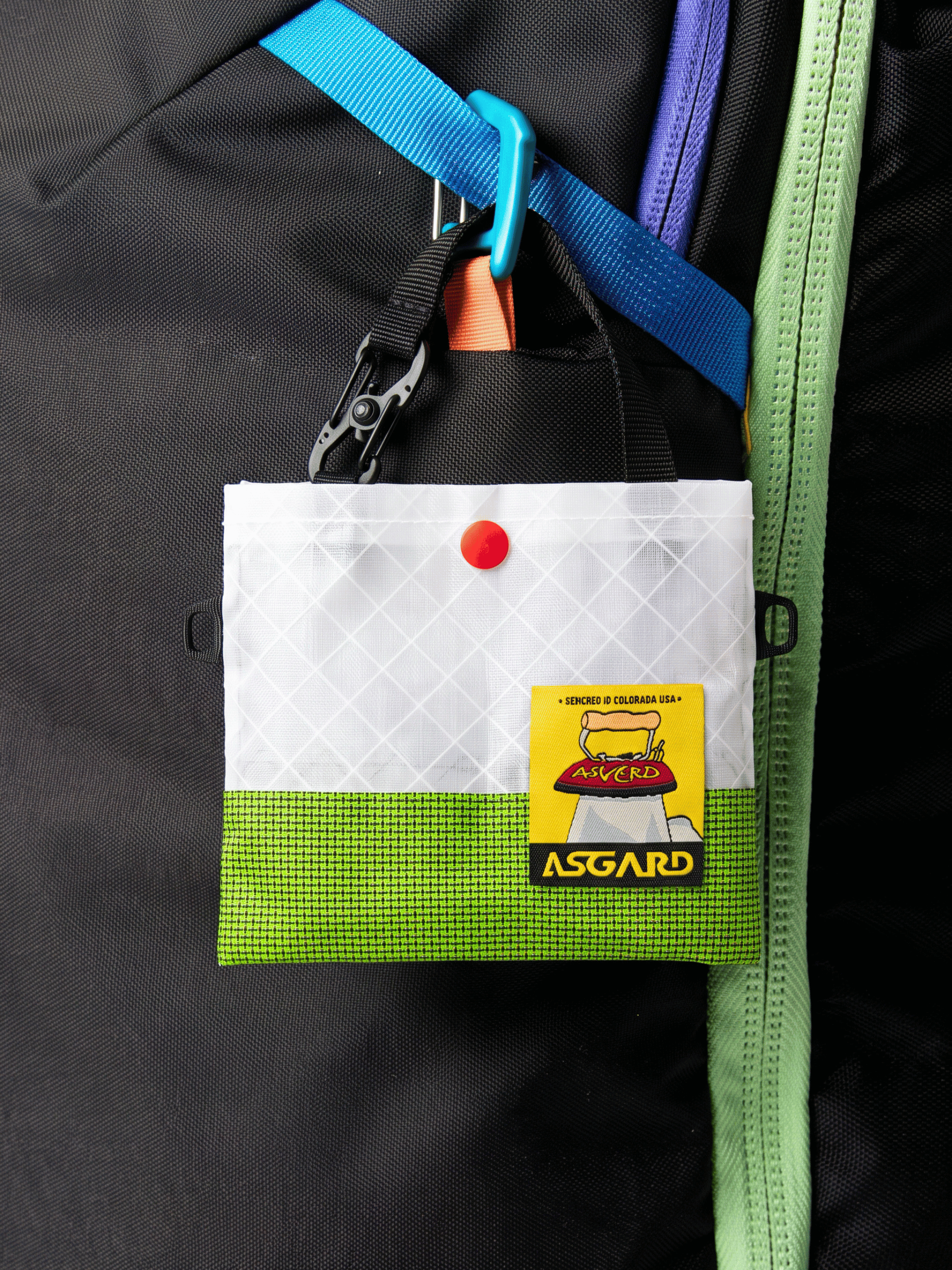 Green Asgard Mini Tote Bag hanging from a blue clip on a black backpack.